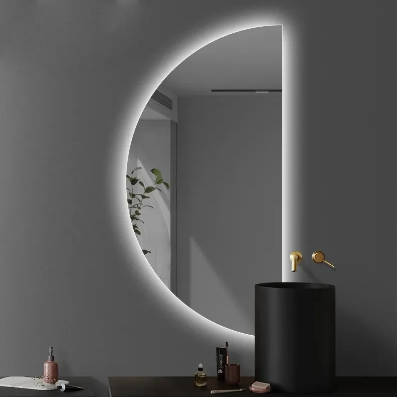 Elegance Luxury Half Moon Glow mirror with cool white backlighting, mounted on a grey wall behind a black pedestal sink.