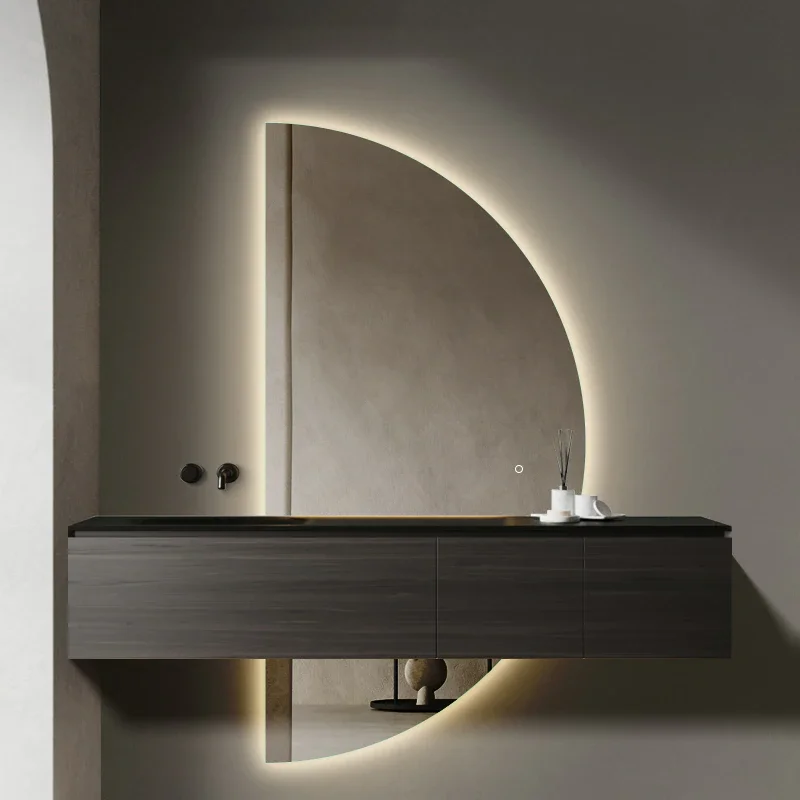 Elegance Luxury Half Moon Glow mirror with warm backlighting, mounted on a dark marble wall behind a black pedestal sink.