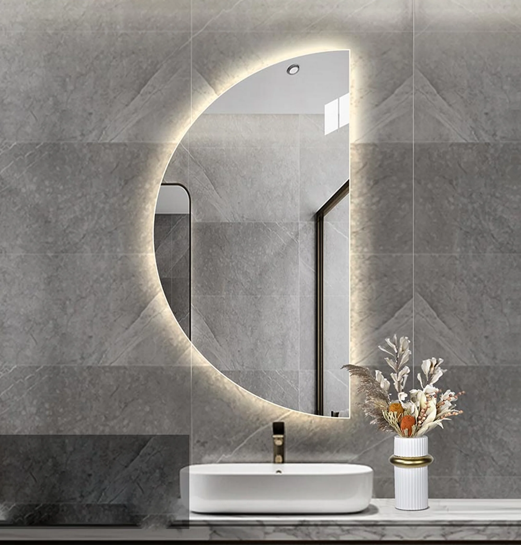 Elegance Luxury Half Moon Glow mirror with warm backlighting, oriented to the left on a grey tiled wall above a white vessel sink.