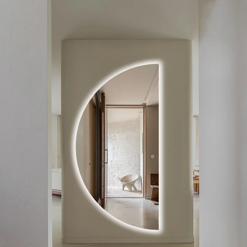 Elegance Luxury Half Moon Glow mirror with cool white backlighting, mounted on a cream-colored pillar in a modern, open hallway.