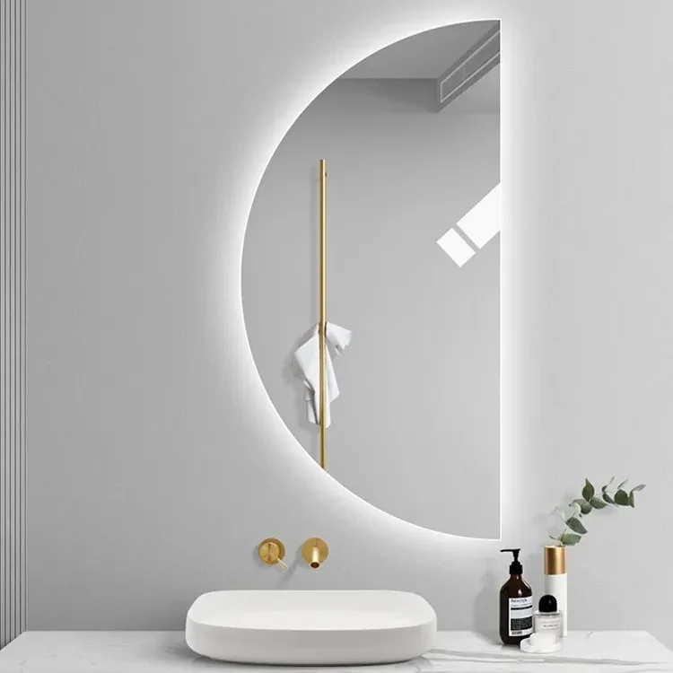 Elegance Luxury Half Moon Glow mirror with cool white backlighting, mounted on a grey wall above a white vessel sink and gold taps.