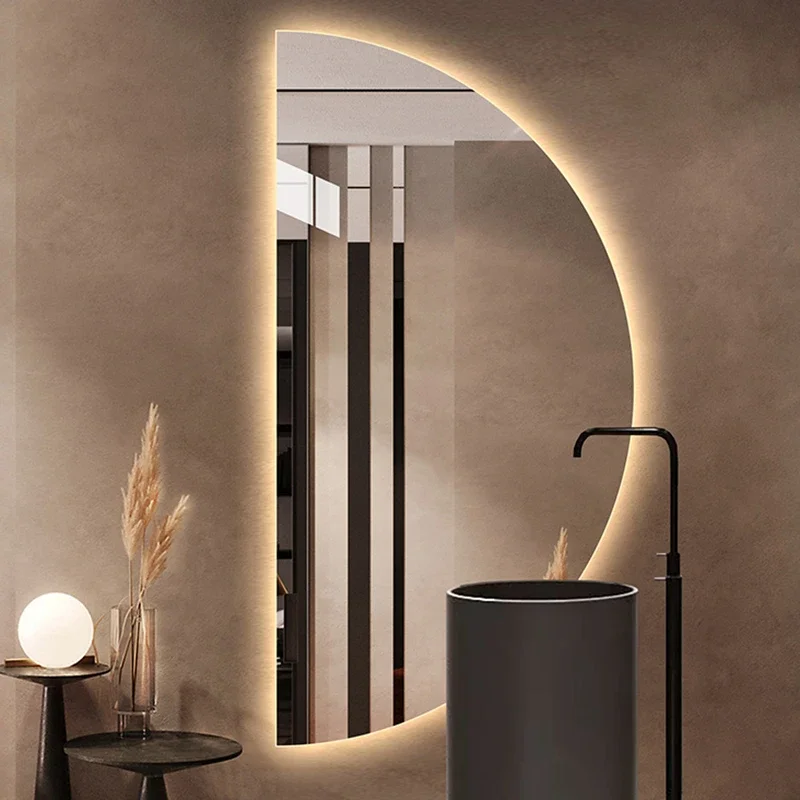 Elegance Luxury Half Moon Glow mirror with warm backlighting, mounted on a textured wall behind a black cylinder pedestal sink.