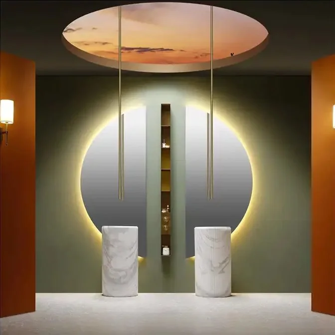 Elegance Luxury Half Moon Glow mirrors flanking a central shelf, with warm backlighting behind marble pedestal sinks.