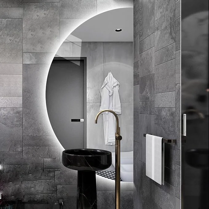 Elegance Luxury Half Moon Glow mirror with cool white backlighting, mounted on a grey stone wall behind a black marble pedestal sink.