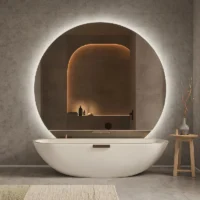 Modern bathroom with round backlit mirror above freestanding tub, warm niche lighting—Statement Mirrors as Decorative Focal Points