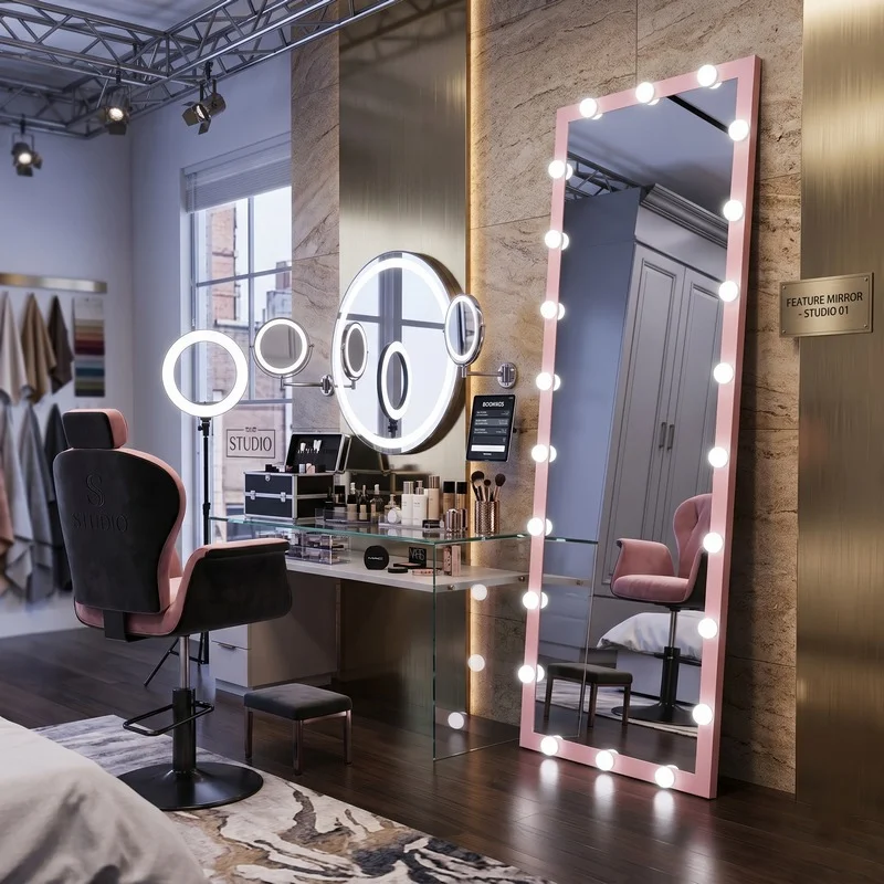 Glam makeup studio with illuminated ring lights, a tall pink-bulb-framed mirror, a round wall mirror, glass vanity with cosmetics, and pink and black chairs.