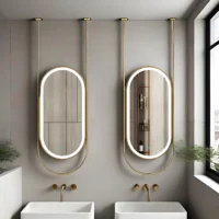 Two gold-framed oval backlit mirrors above white rectangular sinks in a modern bathroom with brass fixtures.