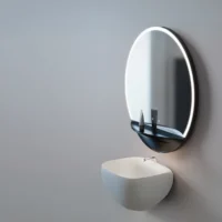 LED Half Moon Round Black Frame Mirror with warm backlighting, mounted on a grey wall above a marble counter and black sink.