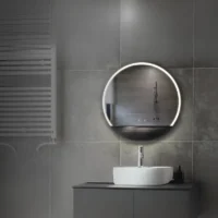 LED Half Moon Round Black Frame Mirror with cool white lighting, mounted on a grey tiled wall above a white sink and black vanity.