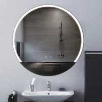 LED Half Moon Round Black Frame Mirror with a cool white glow, mounted on a light grey wall above a modern white pedestal sink.