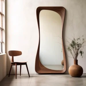 A Japandi Wood Organic Floor Mirror with a thick curved frame, leaning against a white wall next to a wooden chair.
