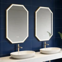 Double vanity with two white oval sinks on a marble countertop, gold-framed octagonal backlit mirrors against a dark blue tiled wall.