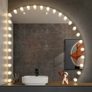1-100285 - Mi-Mirror Round vanity mirror outlined with bright bulbs, lit, above a white sink on a dark marble wall; a small statue and framed art sit on the counter.