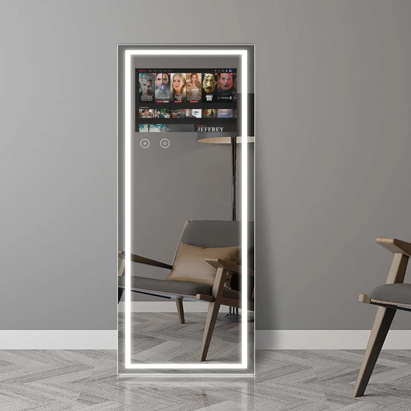 Tall rectangular backlit mirror in a minimalist room, reflecting a beige lounge chair and a wall with a streaming interface visible in the reflection.