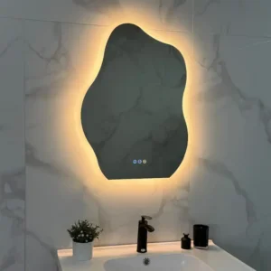 Backlit irregular mirror above a white sink with a black faucet, marble walls, and a small potted plant on the counter.