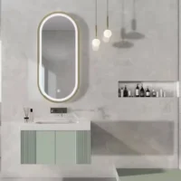 Modern bathroom with an oval backlit mirror above a white sink and mint-green cabinet, marble walls, and pendant lights.