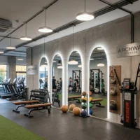 Modern gym interior with mirrors, benches, free weights, and a ball rack; sign reads Archway Fitness in view of workout area.