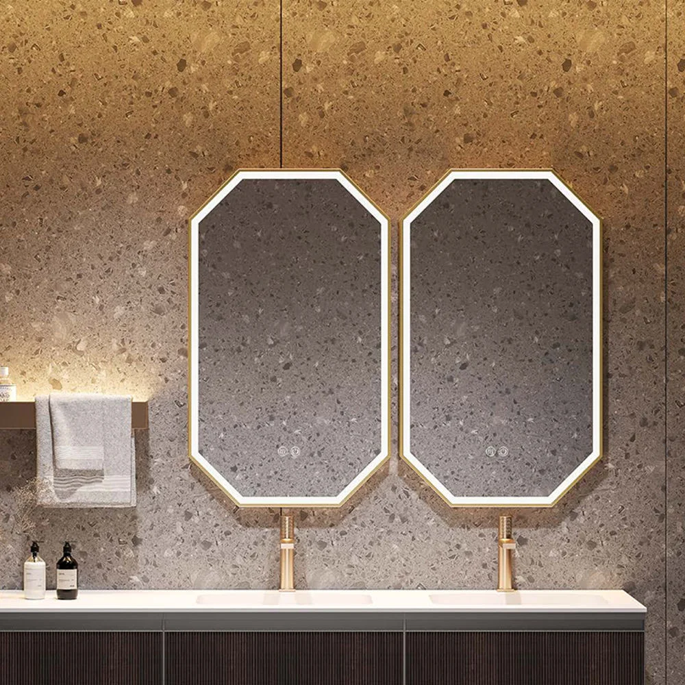 Two octagonal mirrors with gold rims above a white countertop sink in a modern stone bathroom. A towel rack and bottles sit to the left.