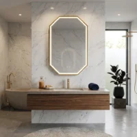 Marble bathroom with a wood vanity, gold faucet, and an illuminated octagonal mirror above a built-in sink area.